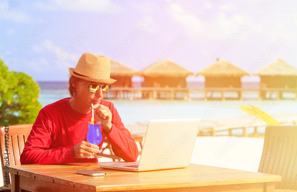 Young man with laptop and cocktail at luxury beach