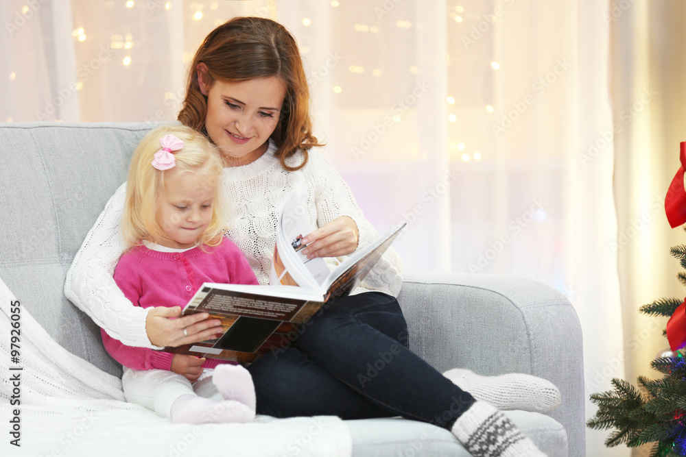 Mum reading book to daughter in Christmas living room