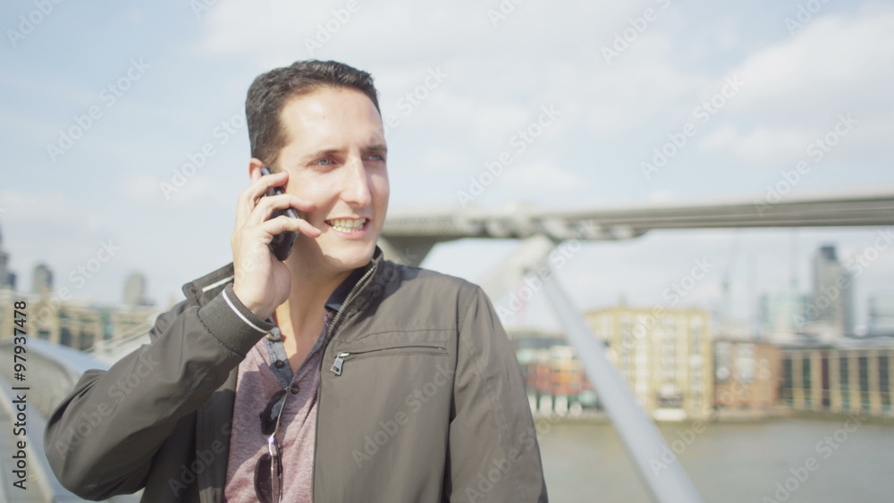 Portrait of casual young man making a phone call in the city with famous London bridge in the background Portrait of casual young man making a phone call in the city with famous London bridge in the background