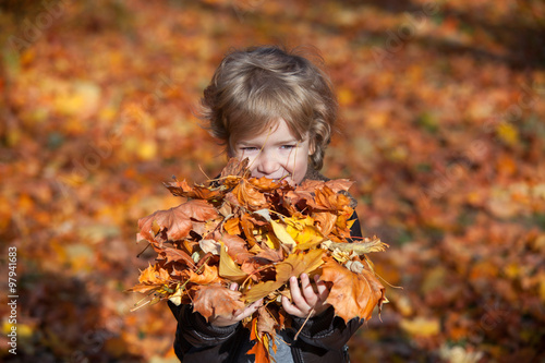 Cute little boy with heap of autumn leaves in his hands.
