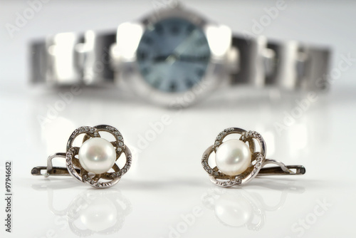 Silver earrings with pearl on the background of watches