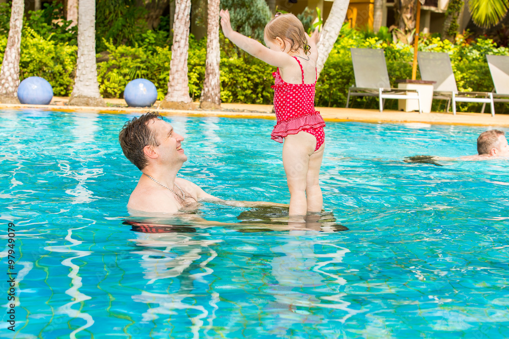 Active father teaching his toddler daughter to swim in pool on tropical resort. Summer vacations and sport  concept