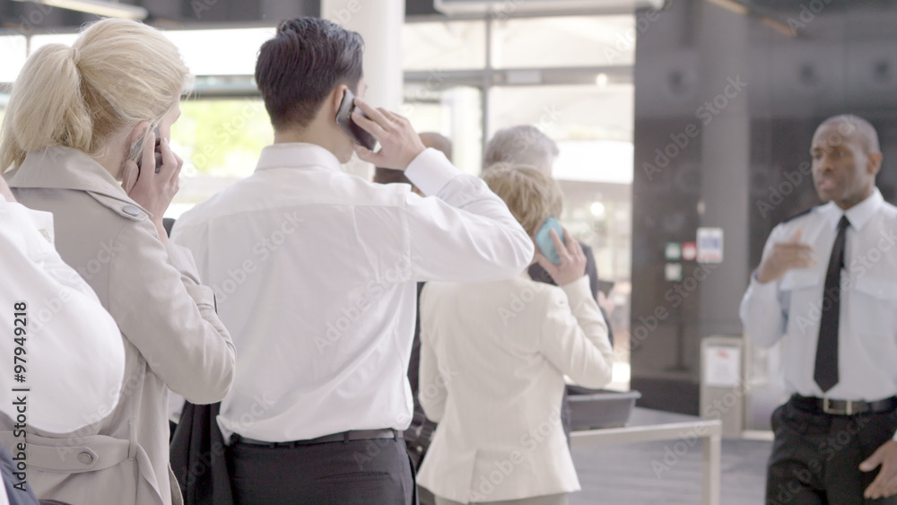 Business people on mobile phones as they wait in queue at airline security Business people on mobile phones as they wait in queue at airline security