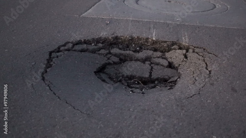 Closeup handheld shot of a dangerously large sinkhole near a manhole cover in an asphalt topped road.