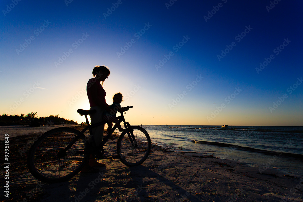 Fototapeta premium Silhouette of mother and baby biking at sunset
