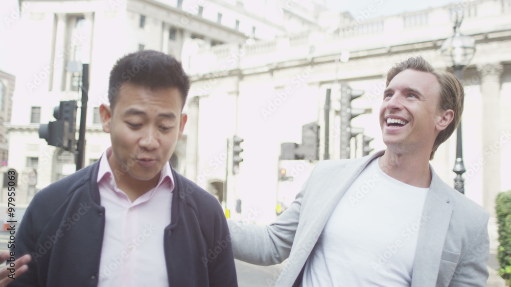Happy casual male friends chatting as they walk through the city Happy casual male friends chatting as they walk through the city