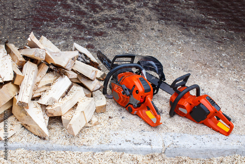 pile of firewood and chainsaw.two chainsaws lying on the ground in the sawdust near with the firewood © EvgeniiAnd