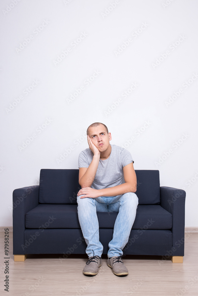 idea concept - thoughtful man sitting on sofa over white wall