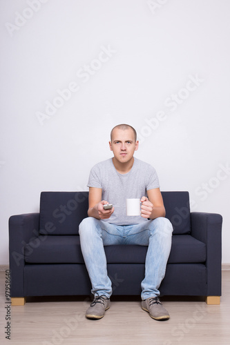 young handsome man sitting on sofa and watching tv with cup of t © Di Studio