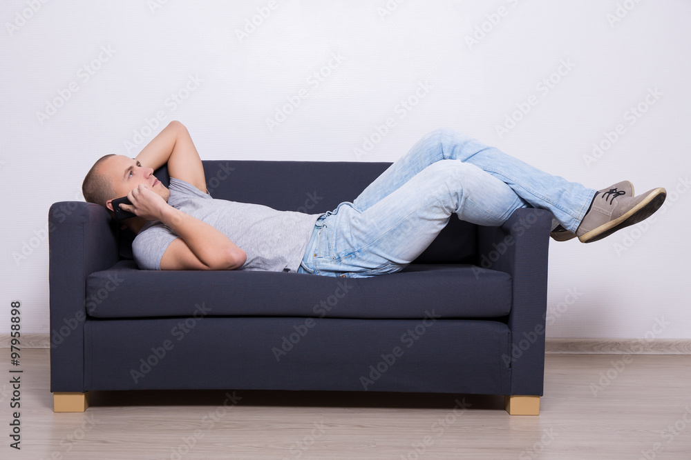 young man lying on sofa and talking on mobile phone young man lying on sofa and talking on mobile phone