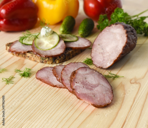 Traditional smoked sausage with dill, sandwich and vegetables on a wooden cutting board
