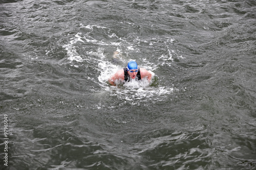 iron man - dynamic and fit swimmer in cap and wetsuit breathing  performing buterfly stroke in dark sea water © endostock