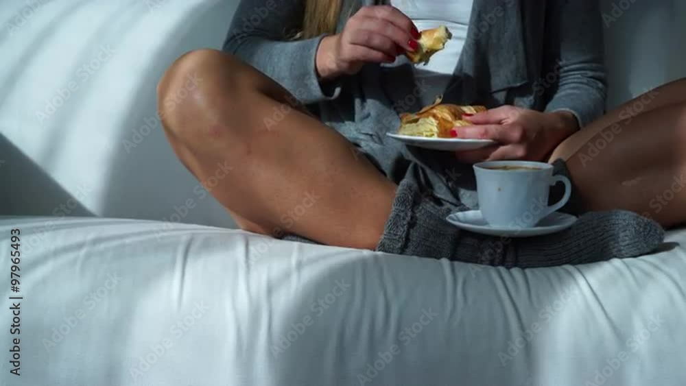 Woman sitting with coffee cup and croissant on couch 4K Woman sitting with coffee cup and croissant on couch 4K