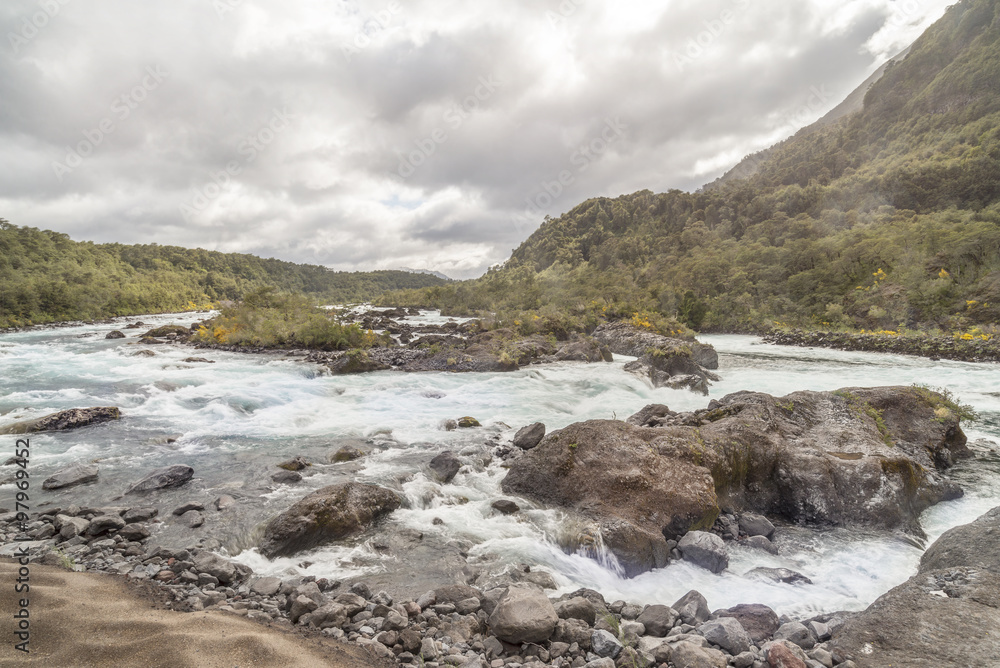 Mountain fast flowing river stream of water in the rocks with cloudy sky