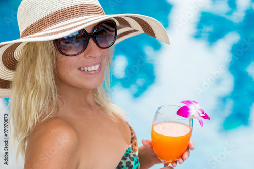 woman in a hat with a glass of orange juice in the pool