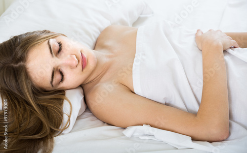 woman lying in bed under sheet with closed eyes