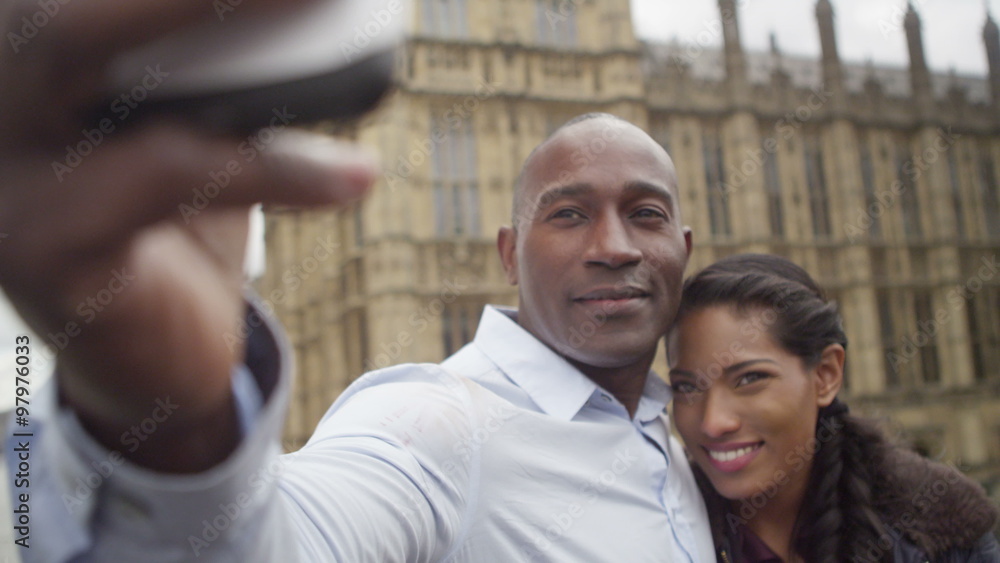 Happy attractive couple sightseeing in London taking a selfie in front of houses of parliament. Happy attractive couple sightseeing in London taking a selfie in front of houses of parliament.