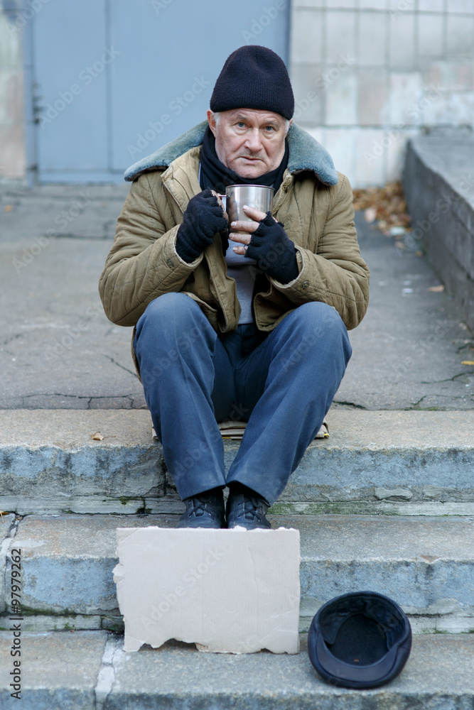 Homeless man holding his iron cup.