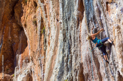 Blond Female Climber ascending Vertical Orange Rock photo