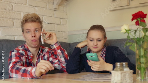 Boy talking on cellphone and girl texting sms in the restaurant
 photo