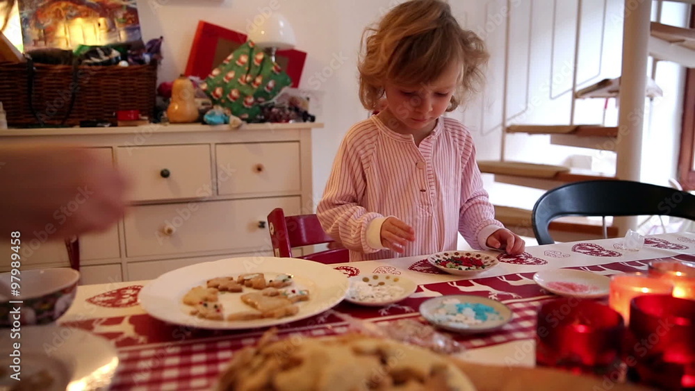 A little girl and her mother sit together to make cookies with burning candles and decoration in the front and back on advent first A little girl and her mother sit together to make cookies with burning candles and decoration in the front and back on advent first