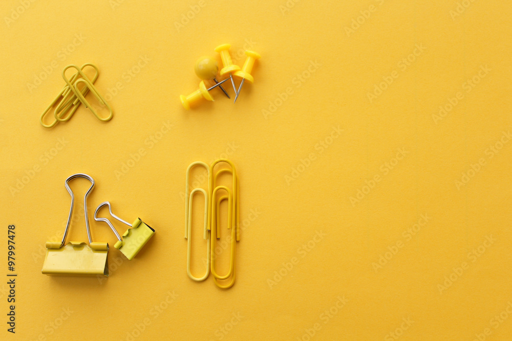 Office supply - binder clip, push pins and paper clip on yellow background Office supply - binder clip, push pins and paper clip on yellow background