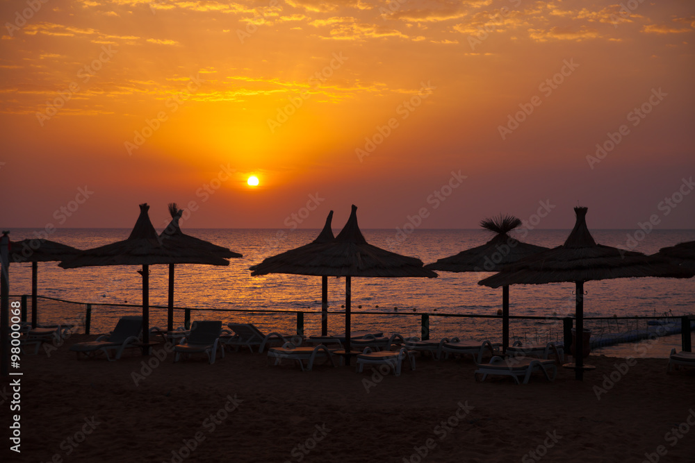 Vacation holidays background wallpaper -  beach lounge chairs under tents on beach. Egypt hotel Sharm El Sheikh at sunset