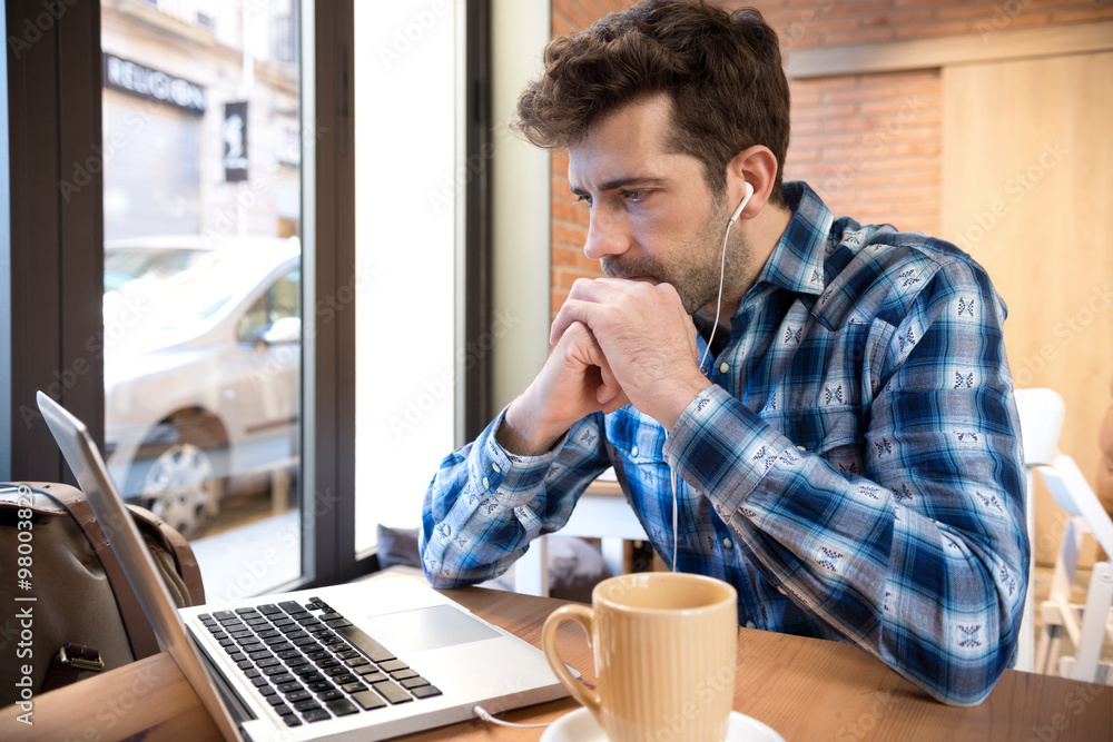 Young man listens to and watches computer with cup you or coffee