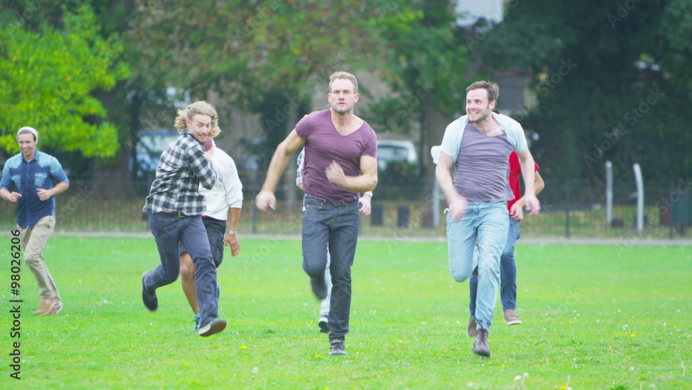 Happy energetic young male friends playing rugby or American football in the park Happy energetic young male friends playing rugby or American football in the park
