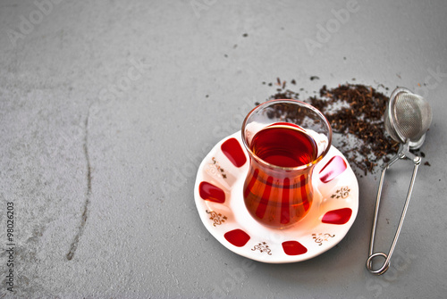 Turkish tea in traditional glass and tea strainer in a pile of tea leaves on a gray background. Top view photo