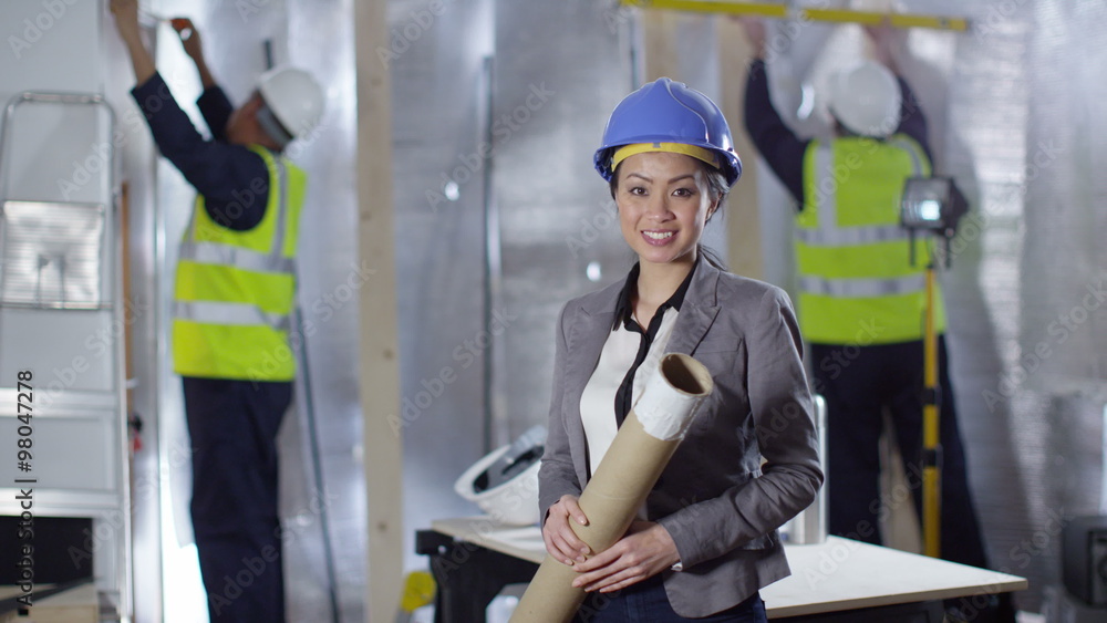  Portrait of smiling female engineer or architect at construction site with building crew working. 
