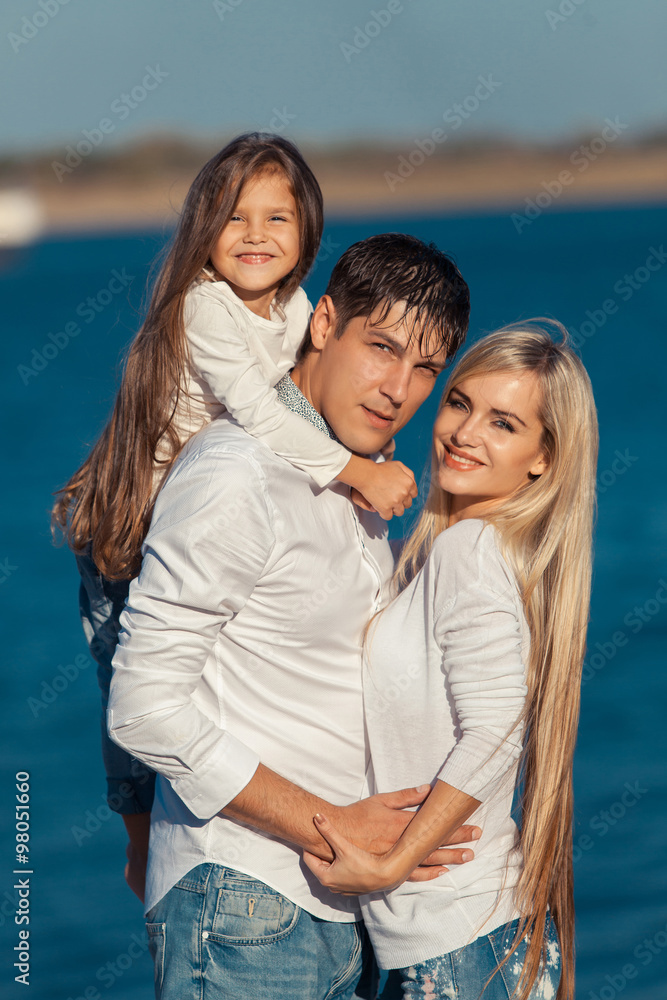 Young family in blue jeans hugging on the background of water Young family in blue jeans hugging on the background of water