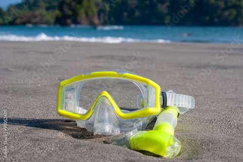 Yellow Scuba Mask and Snorkel (off center) on a beach in Costa Rica. Part of Manuel Antonio Rainforest in background. 