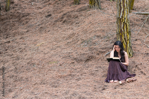 Young woman in long dress reads a book sitting iunder a tree © kiravolkov
