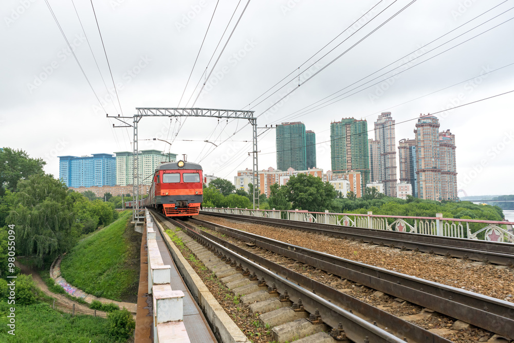 Obraz premium Red and grey suburban electric train moves towards on railroad turn vanishing against skyline background. Moscow, Russia. 