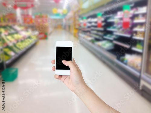 Hand holding mobile phone with Vegetables and fruit on shelf