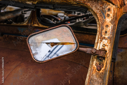 Detail of the wreckage side mirror of an rusty car in garage