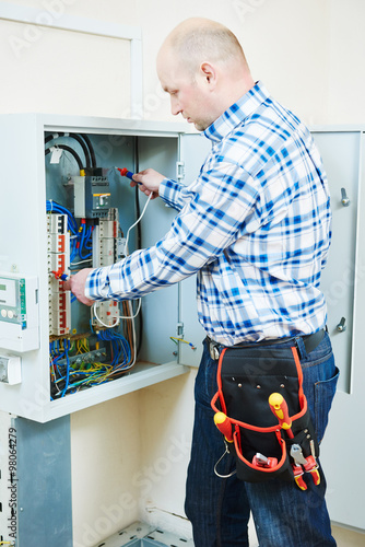 electrician works with electric meter tester in fuse box photo