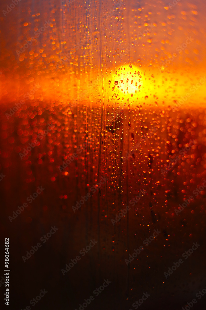 Water drops on a window glass after the rain. The sky with clouds and sun on background.