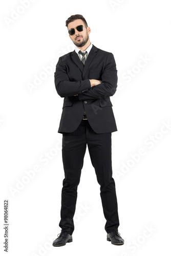 Secret agent or bodyguard with crossed arms looking at camera. Full body length portrait isolated over white studio background.