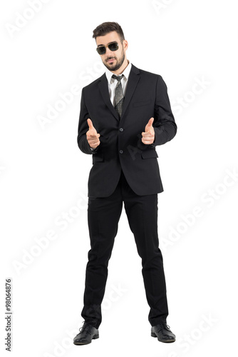 Secret agent with sunglasses aiming hand gun gesture at camera. Full body length portrait isolated over white studio background.