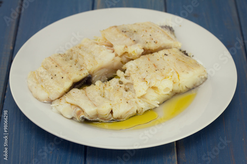 boiled cod fish with olive oil on white plate on blue wooden background