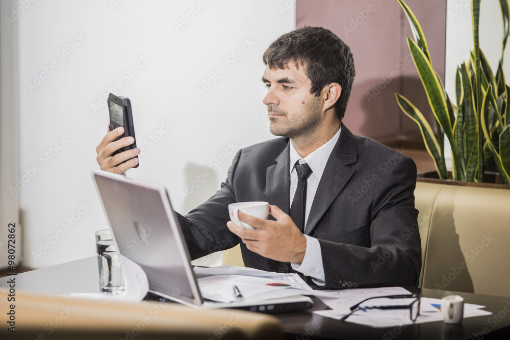 young businessman working at a laptop sitting at a cafe and holding coffee Cup
young businessman working at a laptop sitting at a cafe and holding coffee Cup
