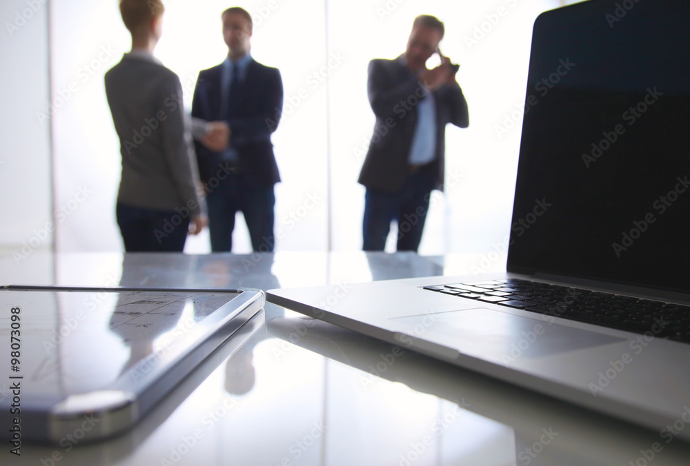 Laptop computer on desk , three businesspeople standing in the background Laptop computer on desk , three businesspeople standing in the background