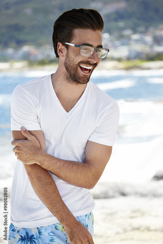 Young man smiling in spectacles and looking away on beach