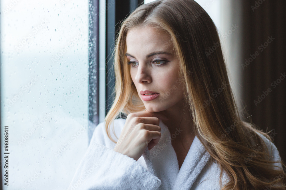 Attractive pensive young female in white bathrobe looking out Attractive pensive young female in white bathrobe looking out