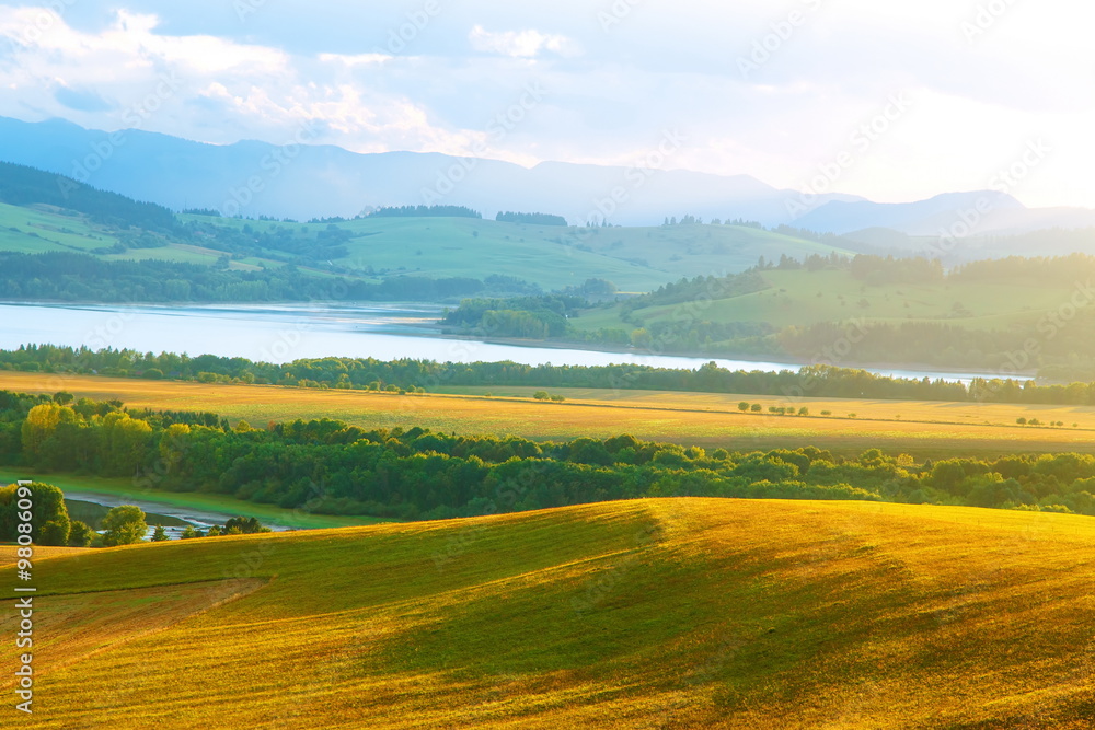 Obraz premium Beautiful landscape, green and yellow meadow and lake with mountain in background. Slovakia, Central Europe.