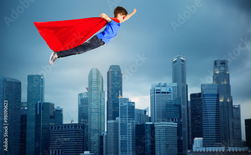 boy in red superhero cape flying over city