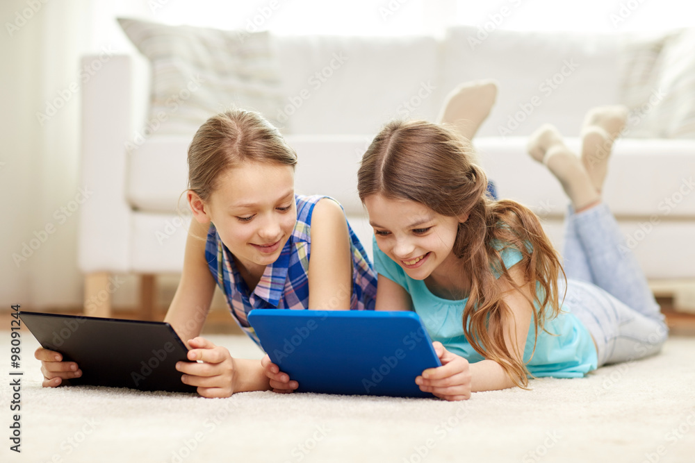 happy girls with tablet pc lying on floor at home