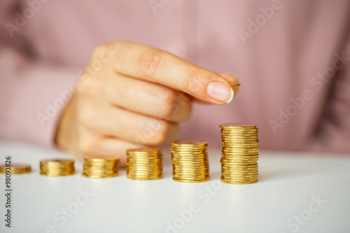 Female hand stacking gold coins into increasing columns